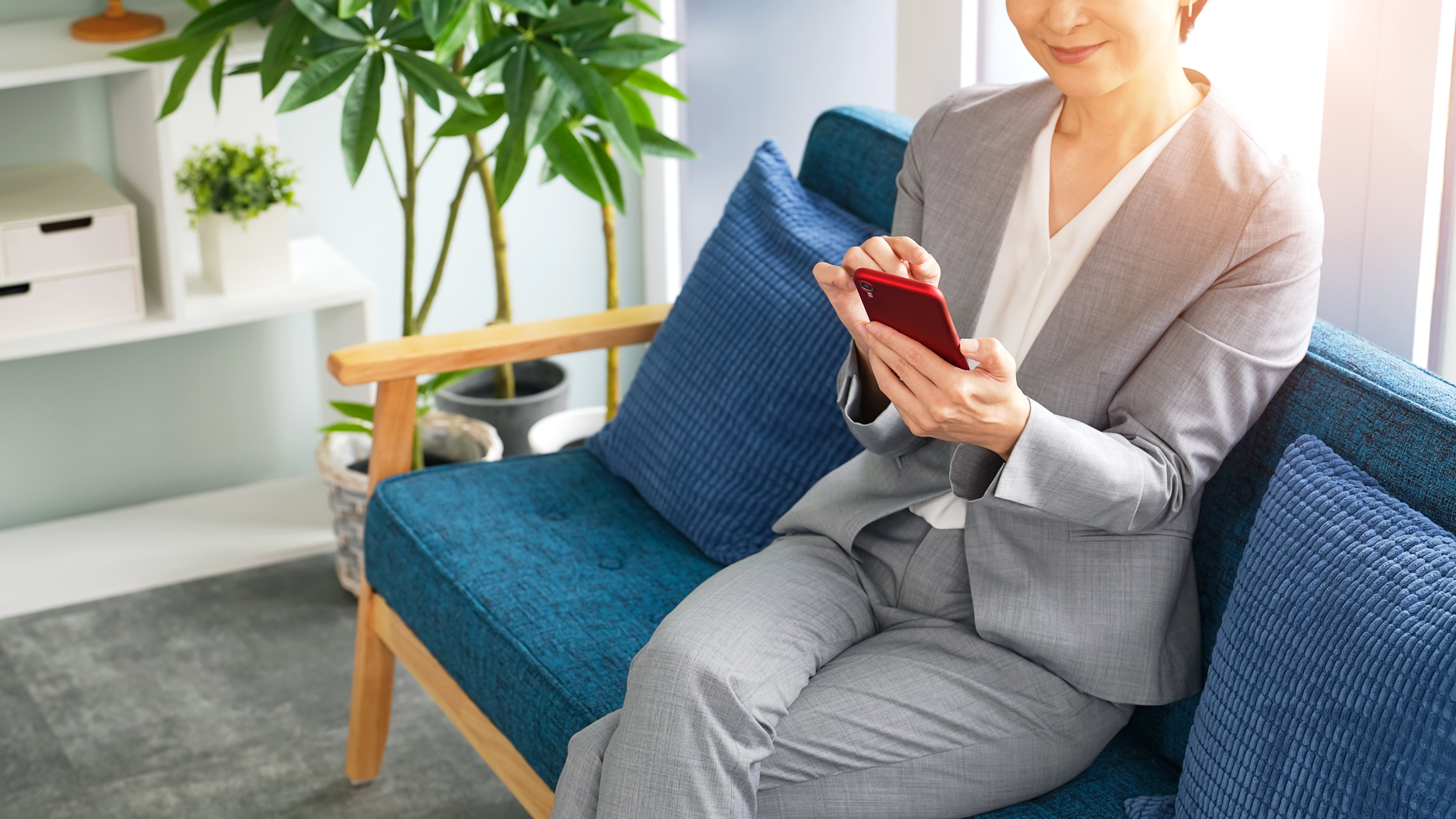ソファでスマートフォンを操作するスーツ姿の女性