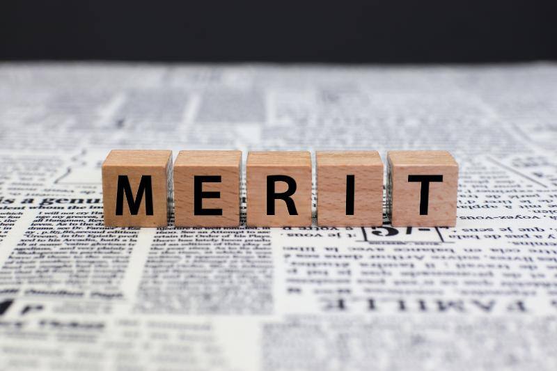 新聞の上に並べられたサイコロにそれぞれ1文字ずつ「MERIT」と書かれた5つのサイコロ
