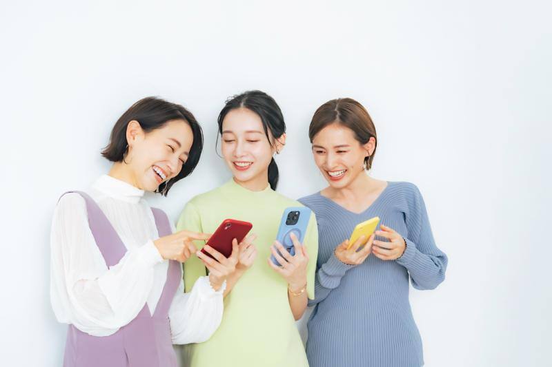 スマートフォンを手に笑顔で会話する女性3人