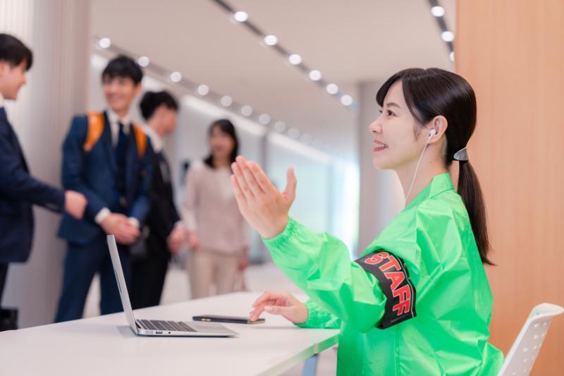 受付で手を挙げて来場者を案内する女性