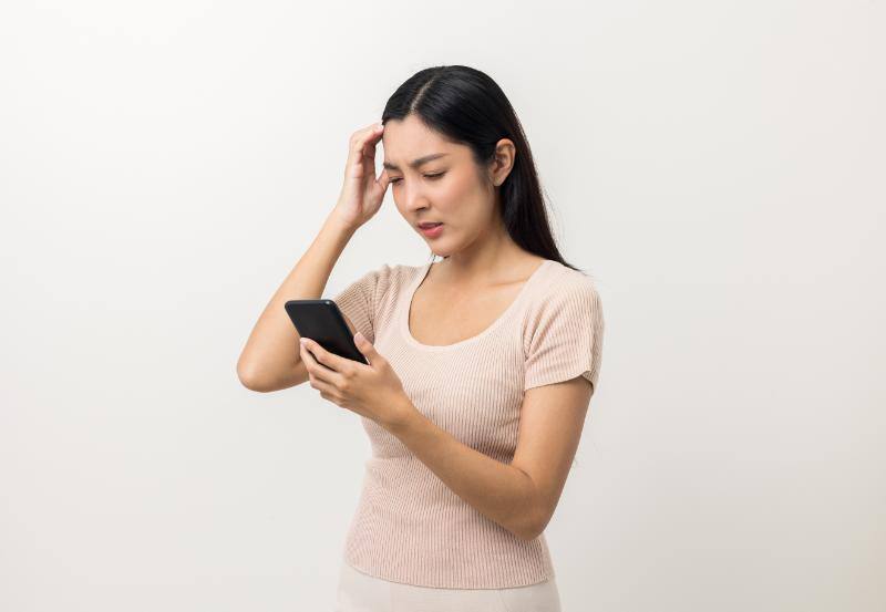 スマホを片手に頭に手を当てて困る女性