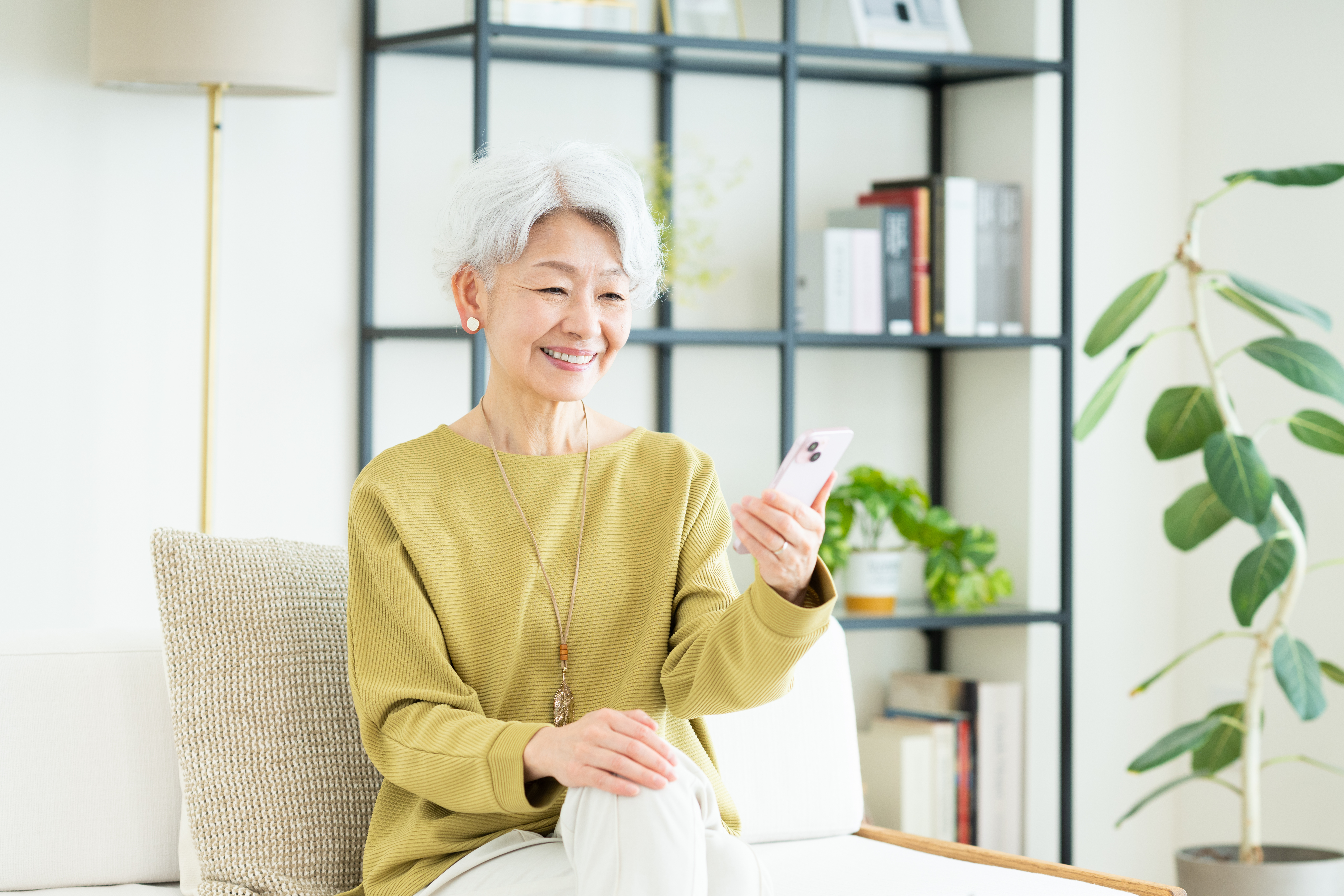 室内でスマートフォンを片手に微笑むシニア女性