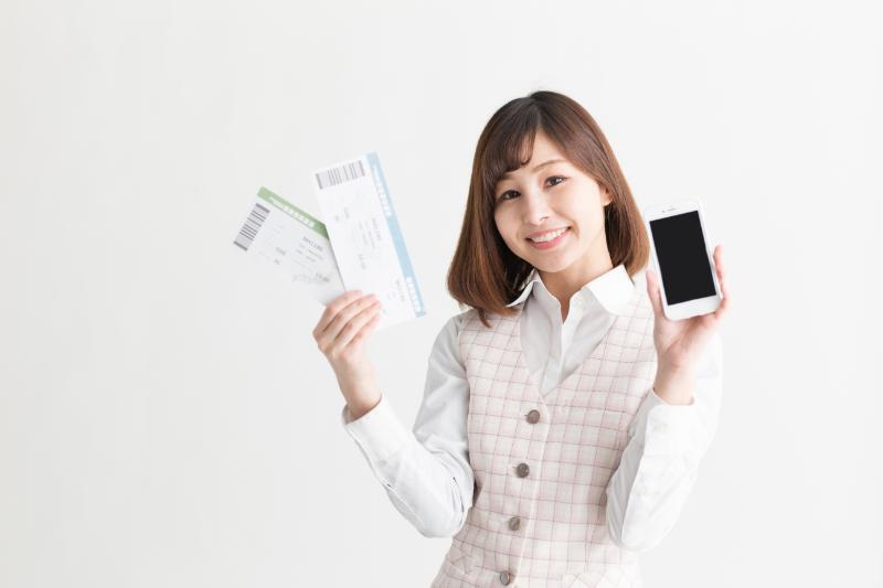 チケットとスマートフォンを両手に掲げる女性