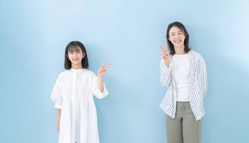 こちらを向いて笑顔でピースサインをしている母と娘