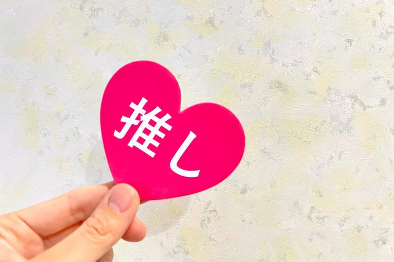 「推し」と書かれたハート型のカードを摘まむ手